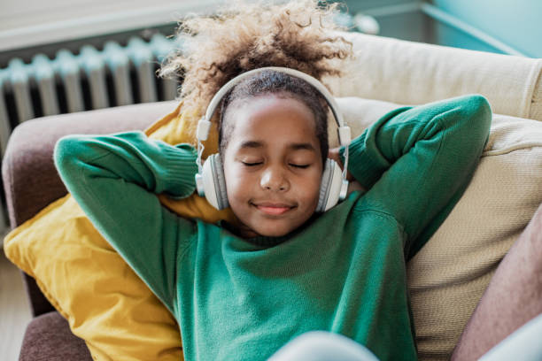Cute little African American girl is listening music at home stock photo