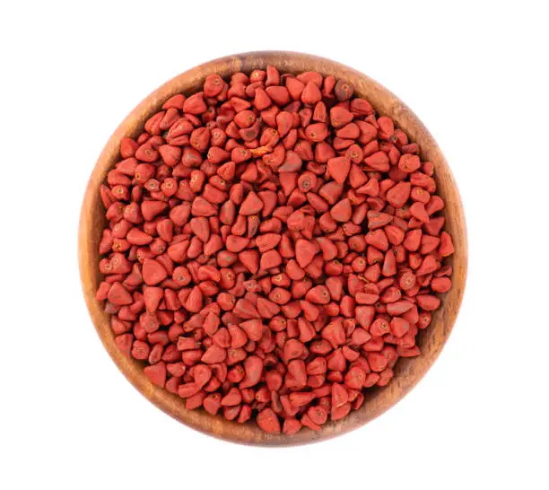 Annatto seeds in wooden bowl, isolated on white background. Achiote seeds, bixa orellana. Natural dye for cooking and food. Top view