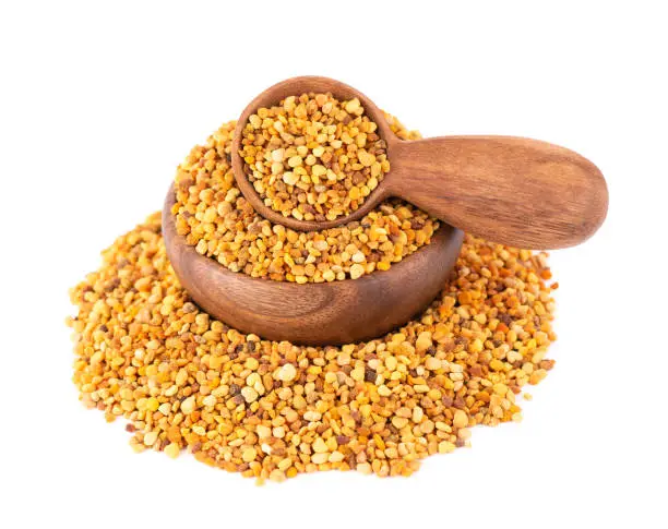 Photo of Flower pollen grains in wooden bowl and spoon, isolated on white background. Pile of bee pollen or perga.