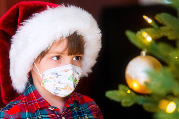 istock Serious Serious pensive Little boy wearing a Santa hat and a protective face mask looking at a Christmas Tree 1281893473
