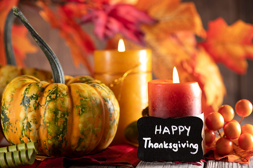 Thanksgiving decoration with pumpkins and candles on illuminated background and a rustic wooden table