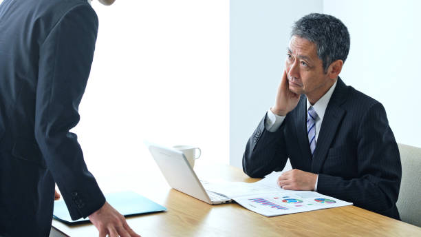 Middle aged asian businessman receiving a report by his subordinate. Middle aged asian businessman receiving a report by his subordinate. subordination stock pictures, royalty-free photos & images