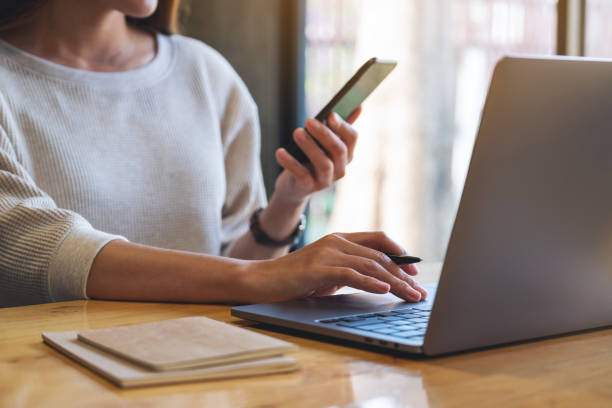 istock a woman holding and using mobile phone and laptop computer in office 1281918526