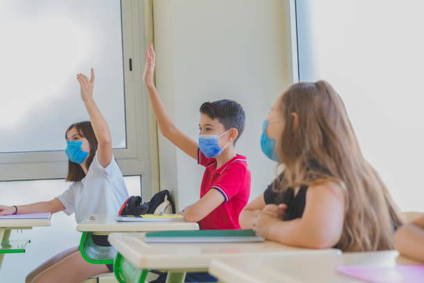 istock Elementary students raising hands during a lesson and wearing face masks 1281926685