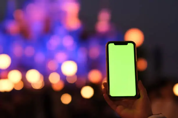 close up one hand showing green screen smart phone in amusement park at night. Beautiful bokeh background