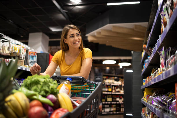 mujer comprando comida en el supermercado. mujer empujando el carro y tomando comida de los estantes. - mercado fotografías e imágenes de stock