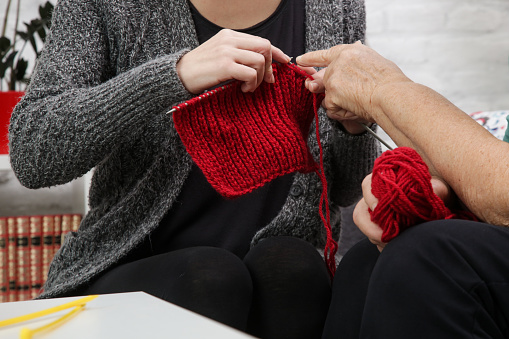Grandomther and granddaughter spending quality time together in creative and fun ways whilst strengthening their family bonds. Senior woman teaching young woman how to knit. Craft and DIY concept.