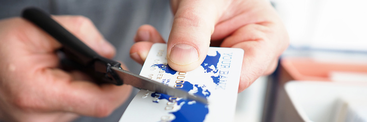 Male hand cutting banking card with scissors closeup