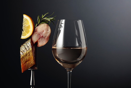 Glass of white wine and smoked mackerel with lemon slice on a dark background. Copy space.
