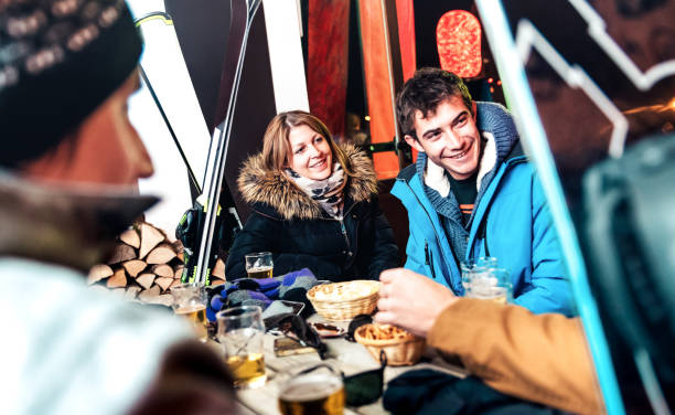 amigos felizes bebendo cerveja e comendo batatas fritas no apreski ao ar livre - jovens se divertindo juntos no restaurante de bar noturno depois de esquiar com equipamento de neve - conceito de amizade com foco na mulher - atividades depois de esquiar - fotografias e filmes do acervo