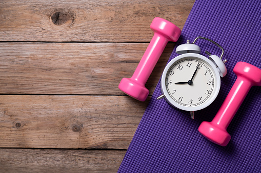 Time for exercising alarm clock and dumbbell with colorful yoga mat background