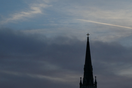 Church spire with cross high up in the sky, silhouette in the morning