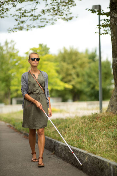 Blind woman walking on city streets, using her white cane Blind woman walking on city streets, using her white cane to navigate the urban space better and to get to her destination safely persons with disabilities photos stock pictures, royalty-free photos & images