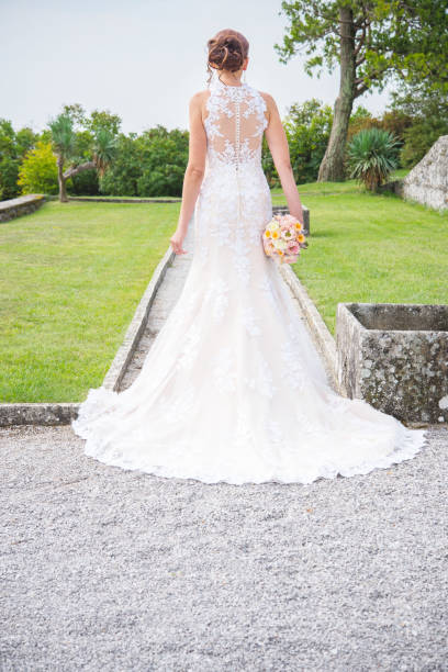 istock Elegant Bride in Wedding Dress Looking at Park Outdoors - Back View 1281960430