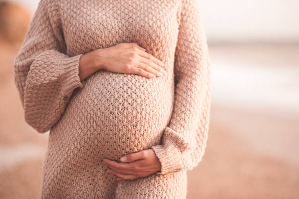 Pregnant woman outdoors over sea Pregnant woman wearing cozy knitted sweater holding tummy with hands outdoors close up. Motherhood. Maternity. Heathy lifestyle. human abdomen photos stock pictures, royalty-free photos & images