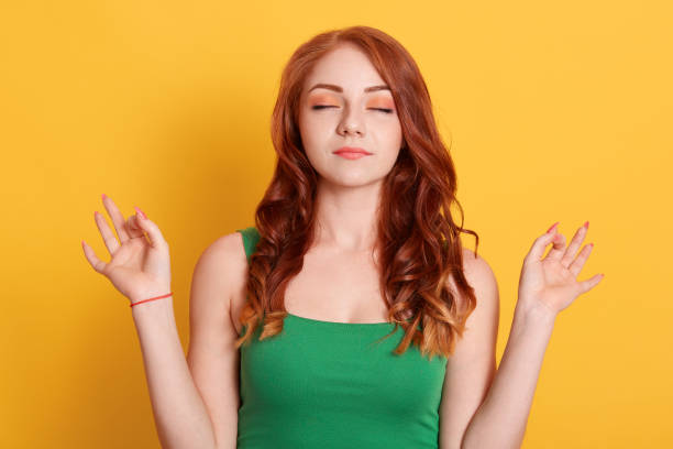 istock Good looking woman meditates, keeps both hands in okay gesture, keeps eyes closed, relaxing after work, practices yoga, wears green shirt, isolated on green wall. 1281975370