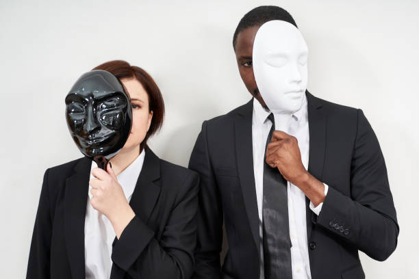 homem africano e mulher caucasiana vestindo ternos pretos escondendo rosto com máscaras plásticas - mask hiding women dishonesty - fotografias e filmes do acervo