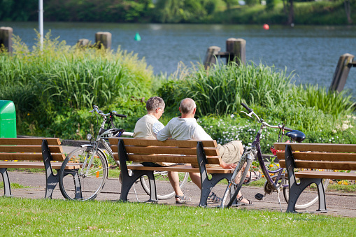 Relaxing mature caucasian couple on bench at river Ruhr in Essen Kettwig in spring season. Scene is at main promenade. At side of bench are bicycles of couple