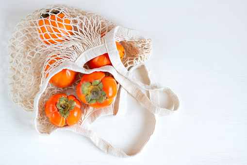 Ripe orange persimmon in a mesh shopping bag on a white background. Copy space for text.