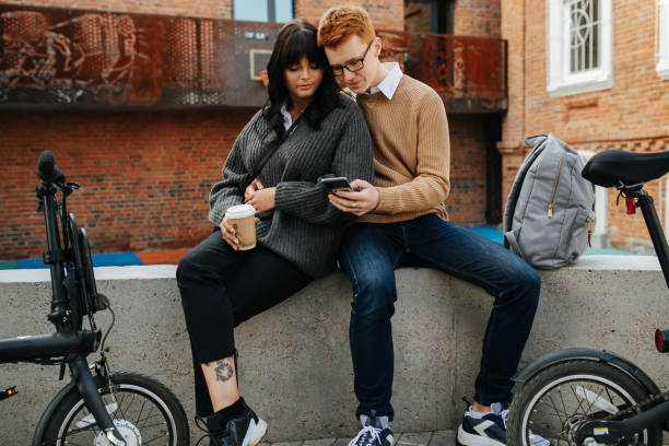 istock Resting young couple, two peaople sitting on a concrete border, looking at phone 1281988369