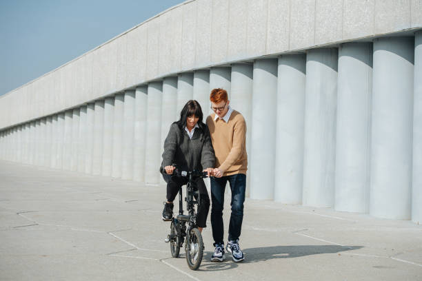 istock Patient young man helping girlfriend ride ebike, supporting her. On a sunny day 1281988433