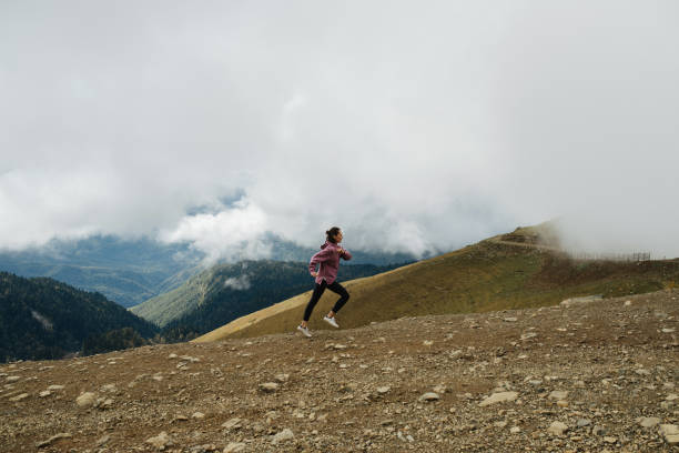 istock Young woman running uphill high up in cloudy mountains. Side view from afar 1281990506