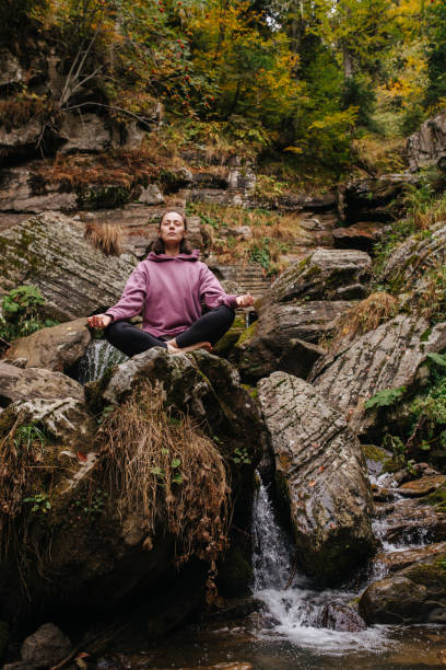 istock Tranquile woman sitting on big stone cross-legged, meditating over spring 1281990515