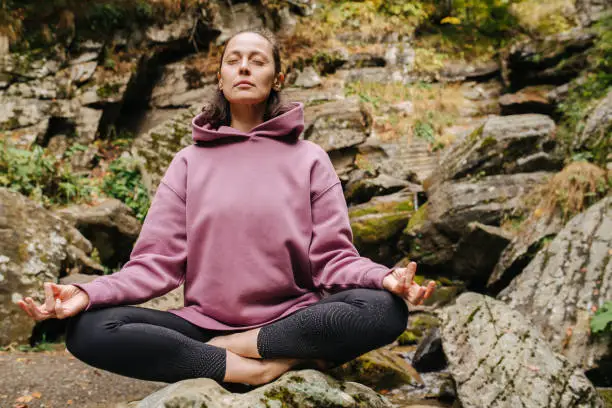 Photo of Peaceful young woman sitting on big stone cross-legged, meditating