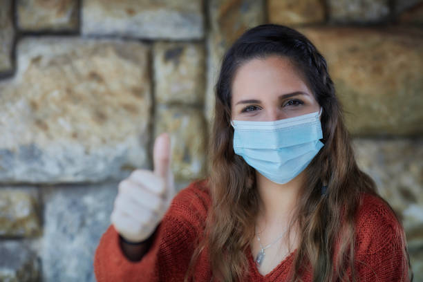 istock Hispanic young woman smiling behind a protective mask with thumb up greeting 1281999436