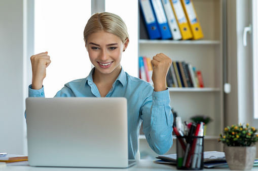 Hhappy young woman celebrating at her desk in a office