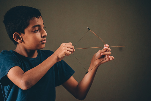 12 year old boy playing with bow and arrow made with stick  inside home India, Karnataka,Mysore,