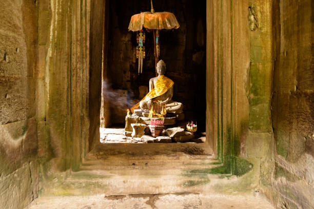 A multi-armed stone statue of Avalokiteshvara (Lokeshvara) stands inside Bayon Temple, part of the Angkor archaeological complex in Cambodia. The ancient Khmer sculpture is draped with a yellow ceremonial cloth, reflecting ongoing Buddhist devotional practices at the historic site. Bayon Temple, built in the late 12th to early 13th century during the reign of King Jayavarman VII, is renowned for its religious symbolism and enduring cultural significance in Southeast Asia.