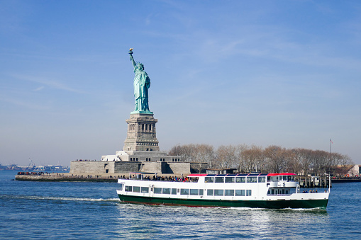 Statue of Liberty in NY Harbor with sight-seeing tourist boat, sunny day, blue sky and water