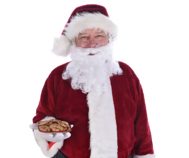 Santa Claus holding a plate full of chocolate chip cookies, isolated on white.