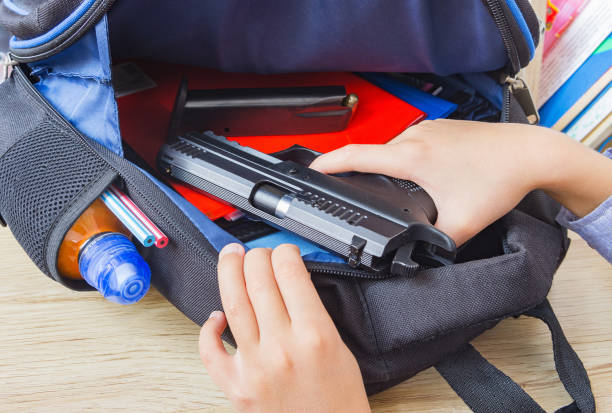 School shootings, gun control concept image. A boy in the classroom pulls out of school backpack a loaded 9mm pistol. School shootings, gun control concept image. A boy in the classroom pulls out of school backpack a loaded 9mm pistol. gun mafia handgun bullet stock pictures, royalty-free photos & images