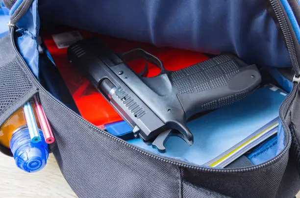 Photo of Loaded 9mm pistol in the school backpack. School shootings, gun control concept image.