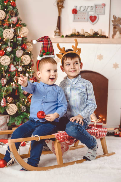 cute and happy little brothers on sleigh having fun - merry christmas - christmas child little boys peeking imagens e fotografias de stock