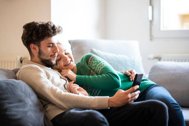 istock Happy young couple relaxing on the sofa while looking at the phone together 1282018963