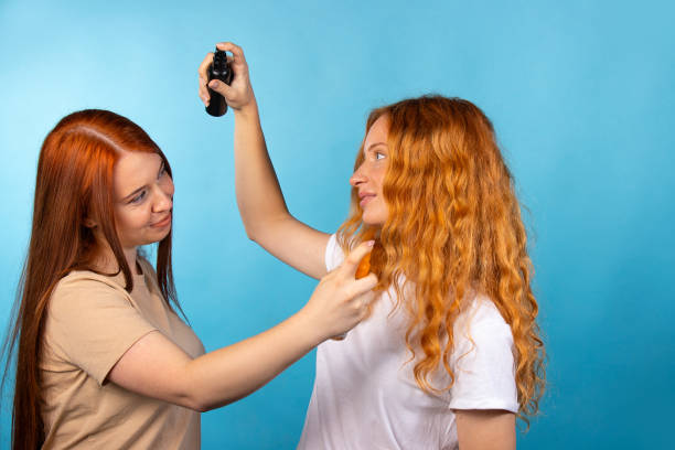 Aroma testing. Long redhaired girls sprays perfume on each other.Hairstyling. Photo on blue background