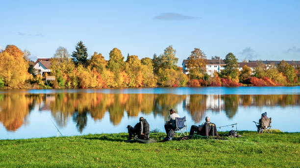 fishermans in foreground,  with beautiful autumn colors reflected in a lake. - black forest forest sky blue imagens e fotografias de stock