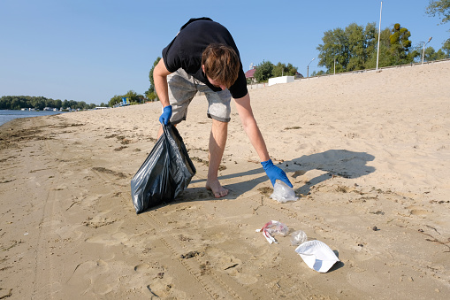 A male volunteer cleaning up trash on the beach. Environmental problems. Environmental protection concept