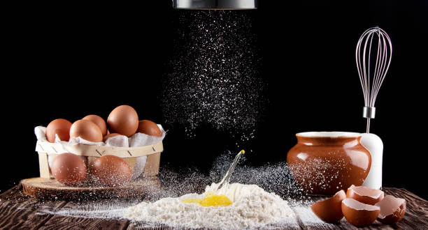 istock Dough preparation. Broken egg falling in flour. Flour is poured on a wooden board with a texture. In the background is a box with eggs, a whisk and a pot. 1282030662