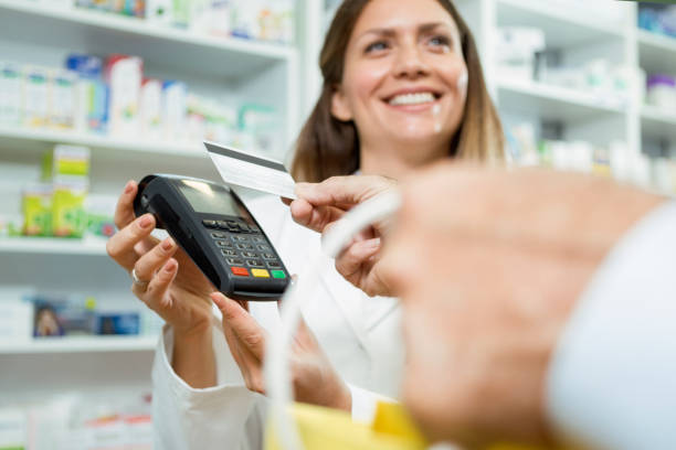 シニア顧客を見ながらクレジットカードリーダーを持っている幸せな女性薬剤師 - credit card reader ストックフォトと画像