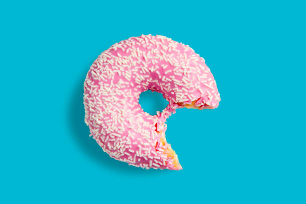 istock One bitten pink donut with white sprinkles on a blue background. Fresh donut poured with pink glaze. 1282032097