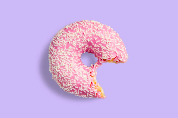 istock One bitten pink donut with white sprinkles on a purple background. Fresh donut poured with pink glaze. 1282032152
