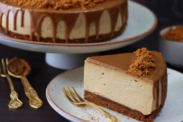 close-up image of toffee caramel cheesecake slice, buttery biscuit base, fluffy mascarpone cream cheese topping covered with toffee caramel sauce, decorated with biscuit crumbs, brown rimmed white plates, marble background, focus on foreground - biscuit brown cake unhealthy eating imagens e fotografias de stock