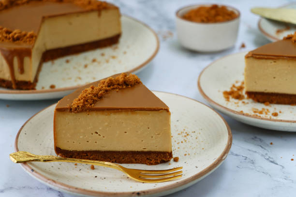 istock Image of sliced toffee caramel cheesecake, buttery biscuit base, fluffy mascarpone cream cheese topping covered with toffee caramel sauce, decorated with biscuit crumbs, brown rimmed white plates, gold cutlery, marble background, focus on foreground 1282034449