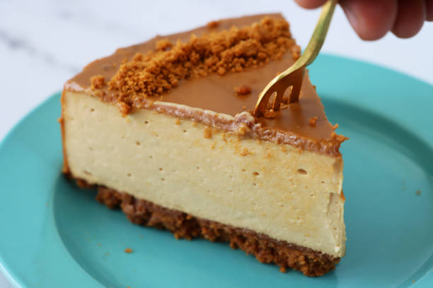 istock Image of unrecognisable person using gold fork to cut into toffee caramel cheesecake slice, buttery biscuit base, fluffy mascarpone cream cheese topping covered with toffee caramel sauce, decorated with biscuit crumbs, turquoise blue plates, marble effect 1282035205