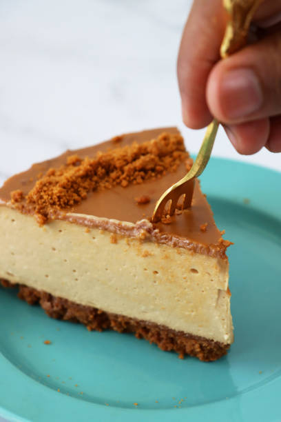 istock Image of unrecognisable person using gold fork to cut into toffee caramel cheesecake slice, buttery biscuit base, fluffy mascarpone cream cheese topping covered with toffee caramel sauce, decorated with biscuit crumbs, turquoise blue plates, marble effect 1282035291