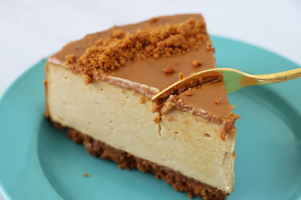 istock Image of gold fork cutting into toffee caramel cheesecake slice, buttery biscuit base, fluffy mascarpone cream cheese topping covered with toffee caramel sauce, decorated with biscuit crumbs, turquoise blue plate, marble effect background 1282035321